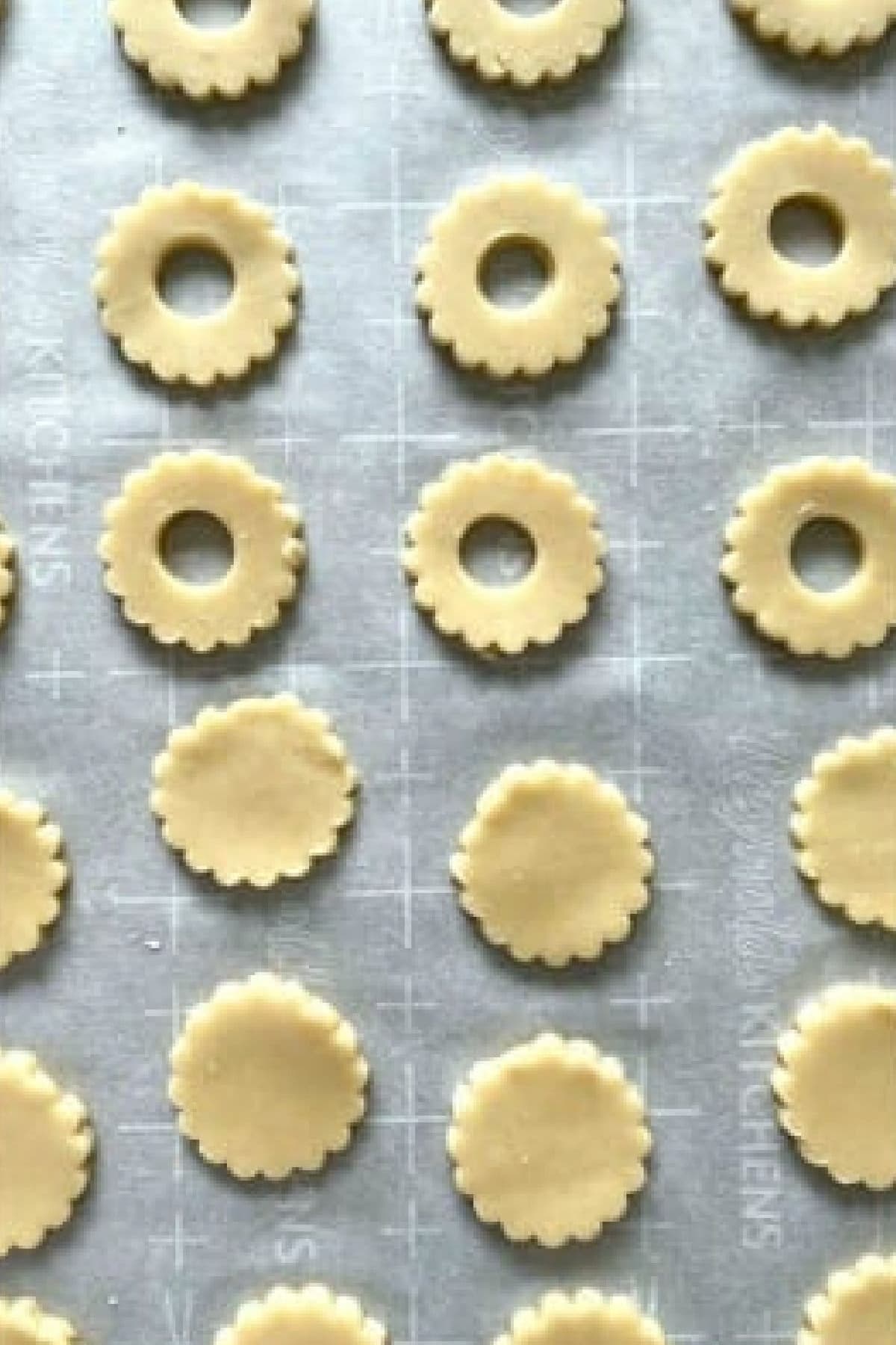 Cookie Dough cut out into scalloped circles and scalloped circles with a hole on a parchment lined baking sheet