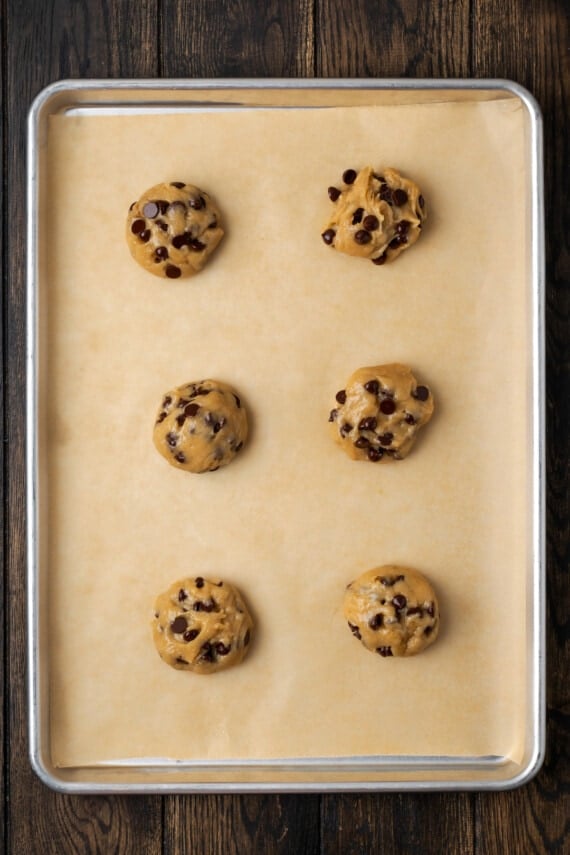 Six unbaked Subway cookie dough balls on a parchment-lined baking sheet.