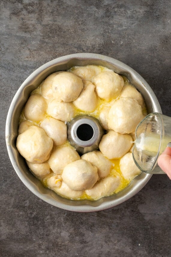 Melted butter poured over top of biscuit dough balls filled with taco filling assembled inside a bundt pan.