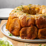 Taco monkey bread topped with melted cheese on a white plate, next to a bowl of shredded lettuce.