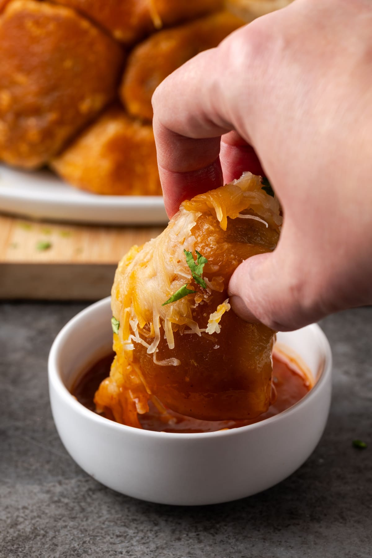 A hand dipping a taco monkey bread bite into a bowl of salsa.