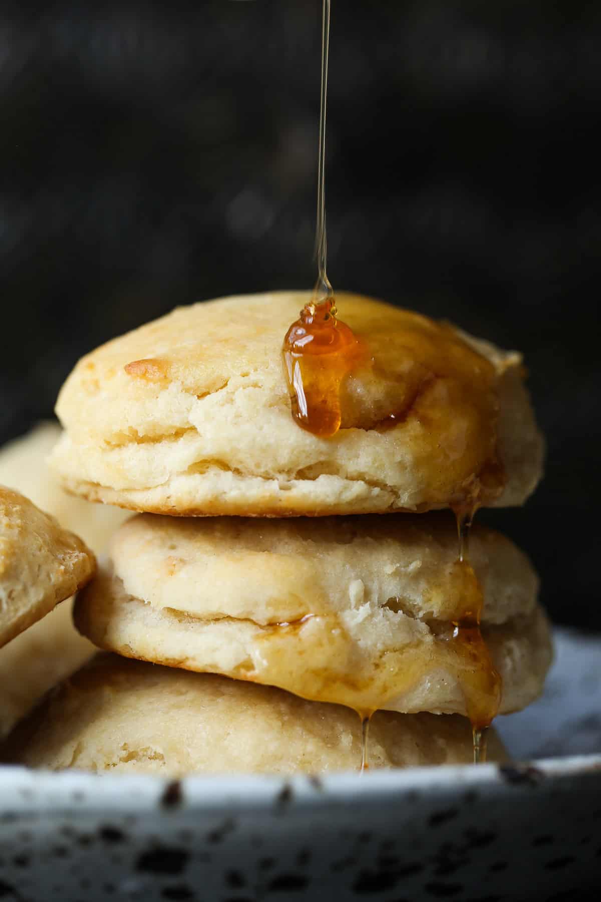 Angel Biscuits stacked on a plate with a drizzle of honey poured on top