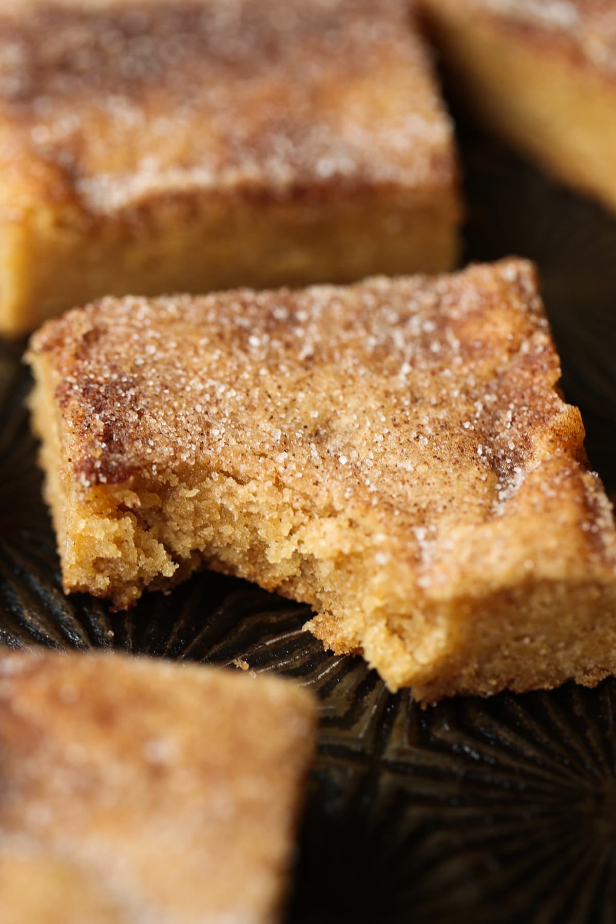 A cinnamon sugar cookie bar with a bite taken out on a baking sheet