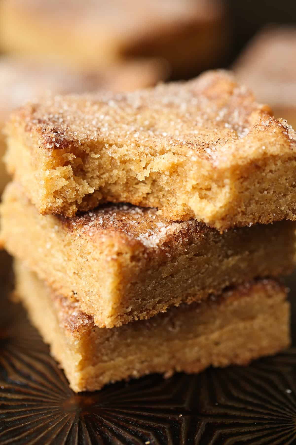 A stack of cinnamon sugar Churro cookie bars stacked with a bite taken from the top one.