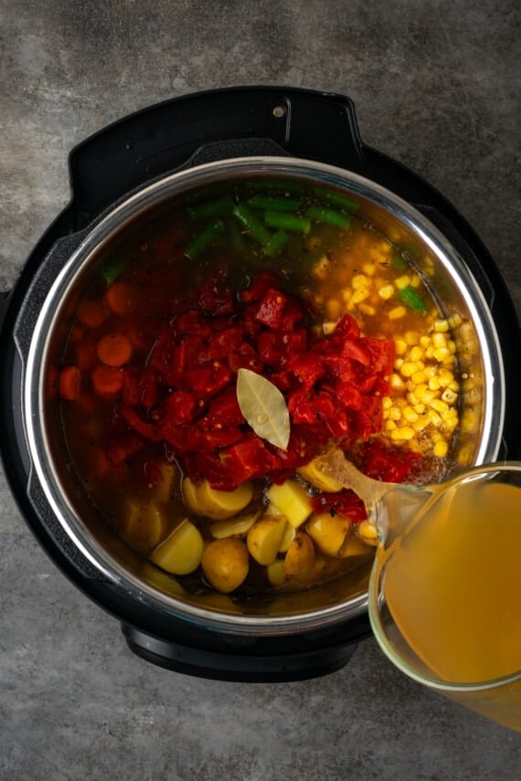 Broth is poured over vegetable soup ingredients inside the instant pot.