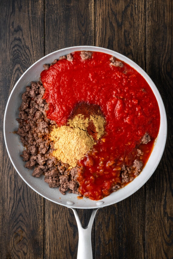 Salsa, crushed tomatoes, and seasonings added to a skillet with browned ground beef.