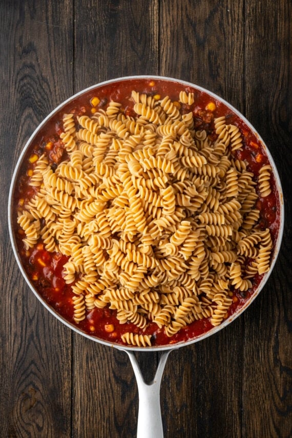 Cooked rotini pasta added to a pan with the taco meat mixture.