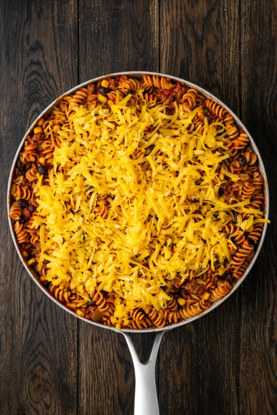 Taco pasta topped with shredded cheese in a large skillet.