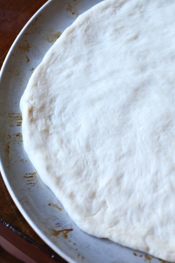 Pizza dough spread out onto a large round baking pan.