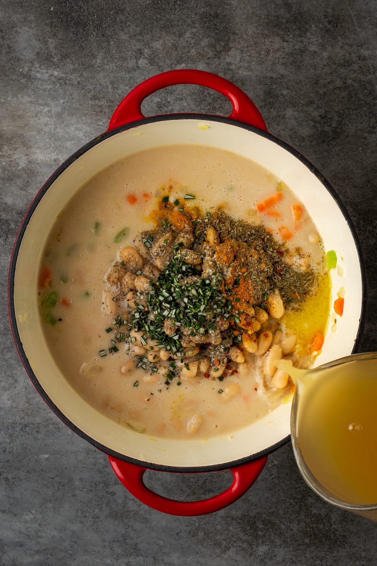 Broth poured into a large pot with white bean soup ingredients.