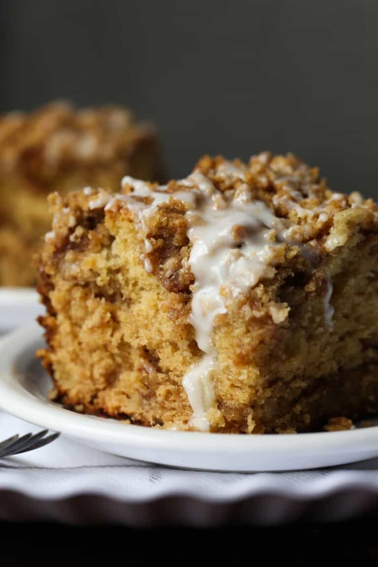 A slice of apple cake on a white plate topped with a thin layer of white glaze icing