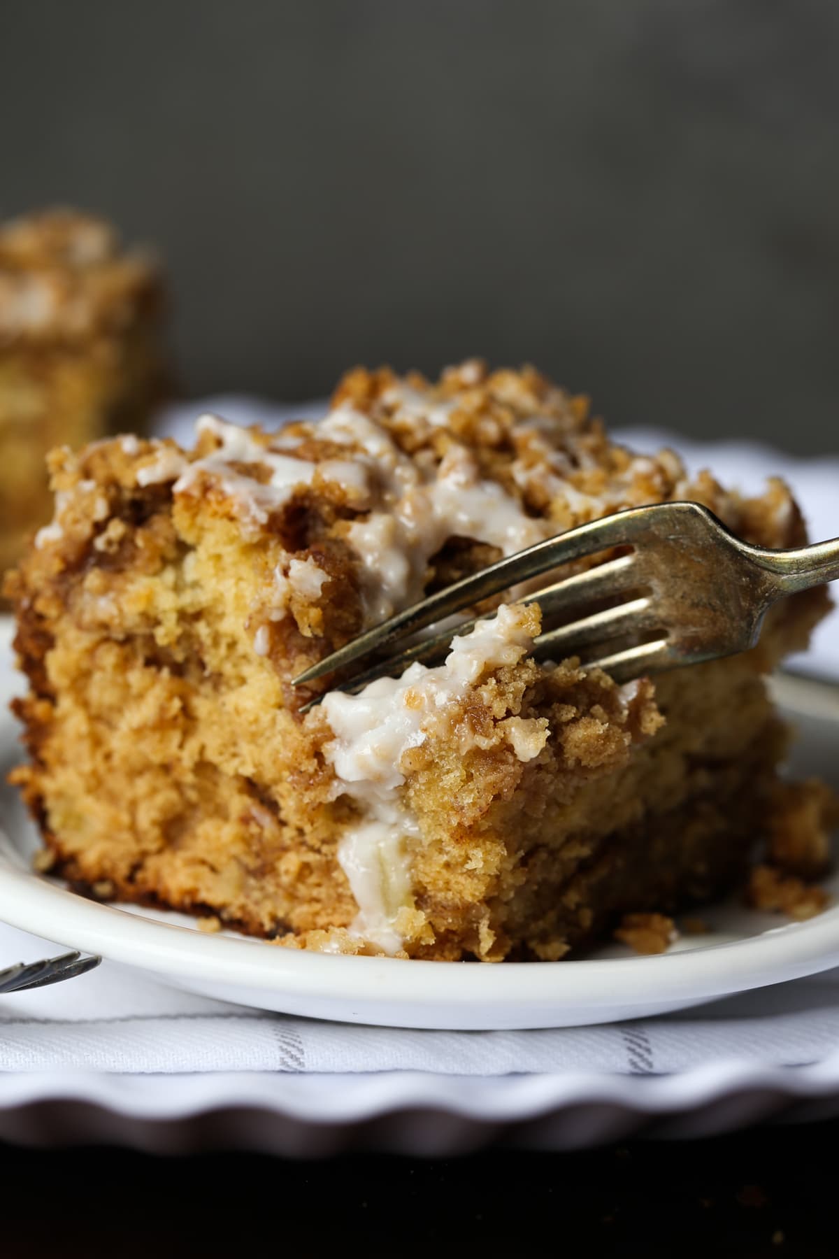 A slice of apple coffee cake on a plate with a fork taking a bite.