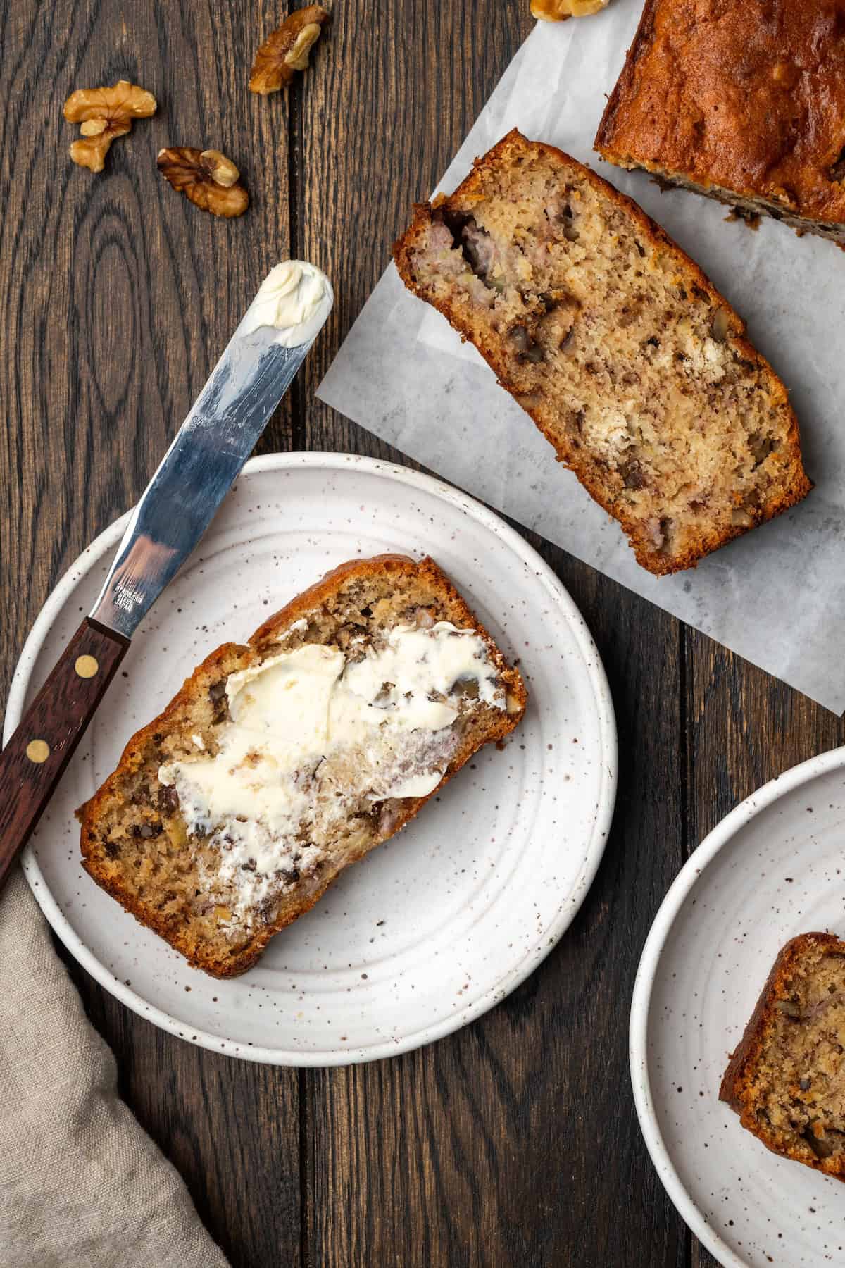 Overhead view of a buttered slice of banana bread on a plate.