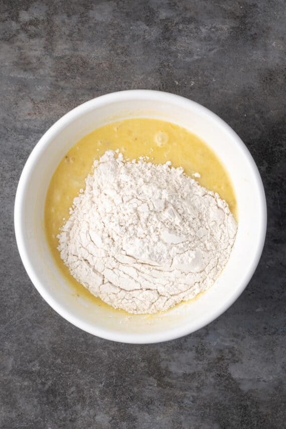 Dry ingredients added to wet banana bread batter in a bowl.