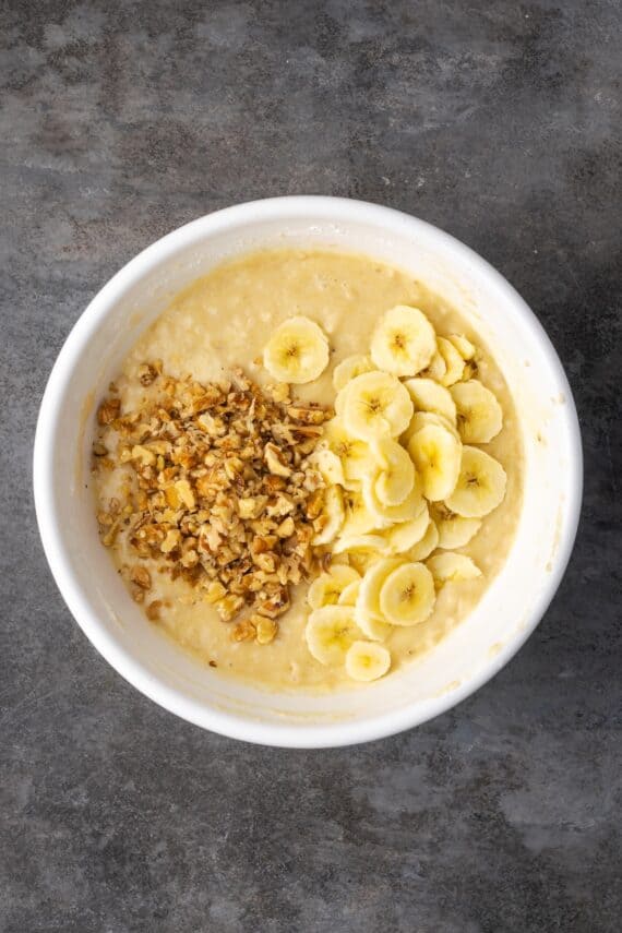 Sliced bananas and walnuts added to banana bread batter in a bowl.