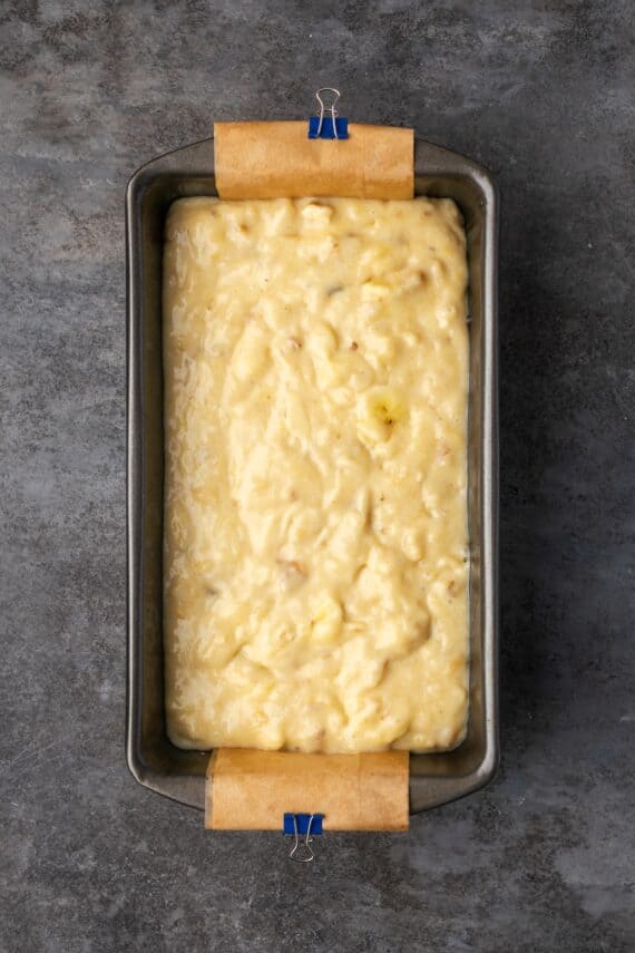 Banana bread batter inside a lined loaf pan.