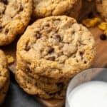 A stack of crunchy, buttery cornflake cookies next to a glass of milk.