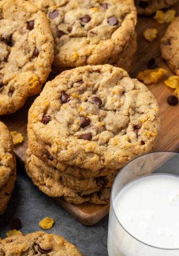 A stack of crunchy, buttery cornflake cookies next to a glass of milk.