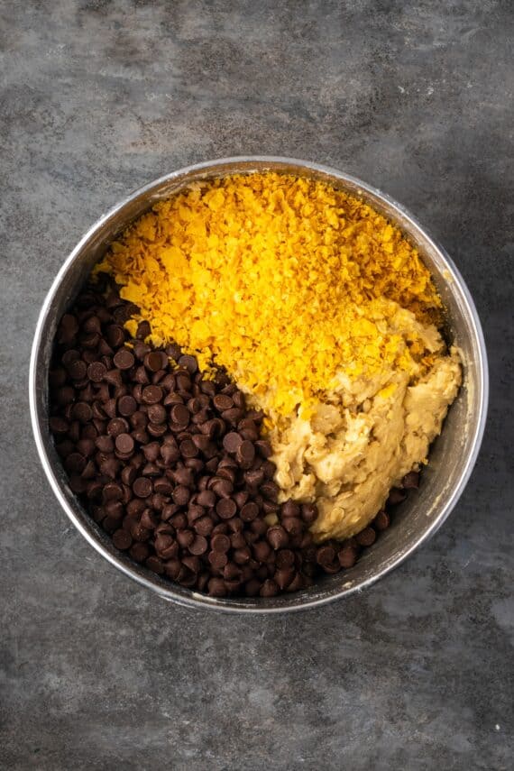 This easy cornflake cookies recipe makes chewy, buttery cookies packed with gooey chocolate chips and nostalgic cornflake cereal crunch! Cornflakes and chocolate chips added to cookie dough in a bowl.