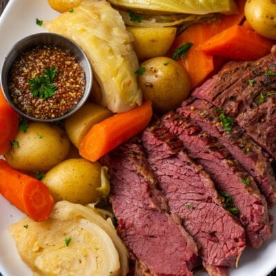 Overhead view of sliced corned beef on a plate next to cabbage, potatoes, and carrots.