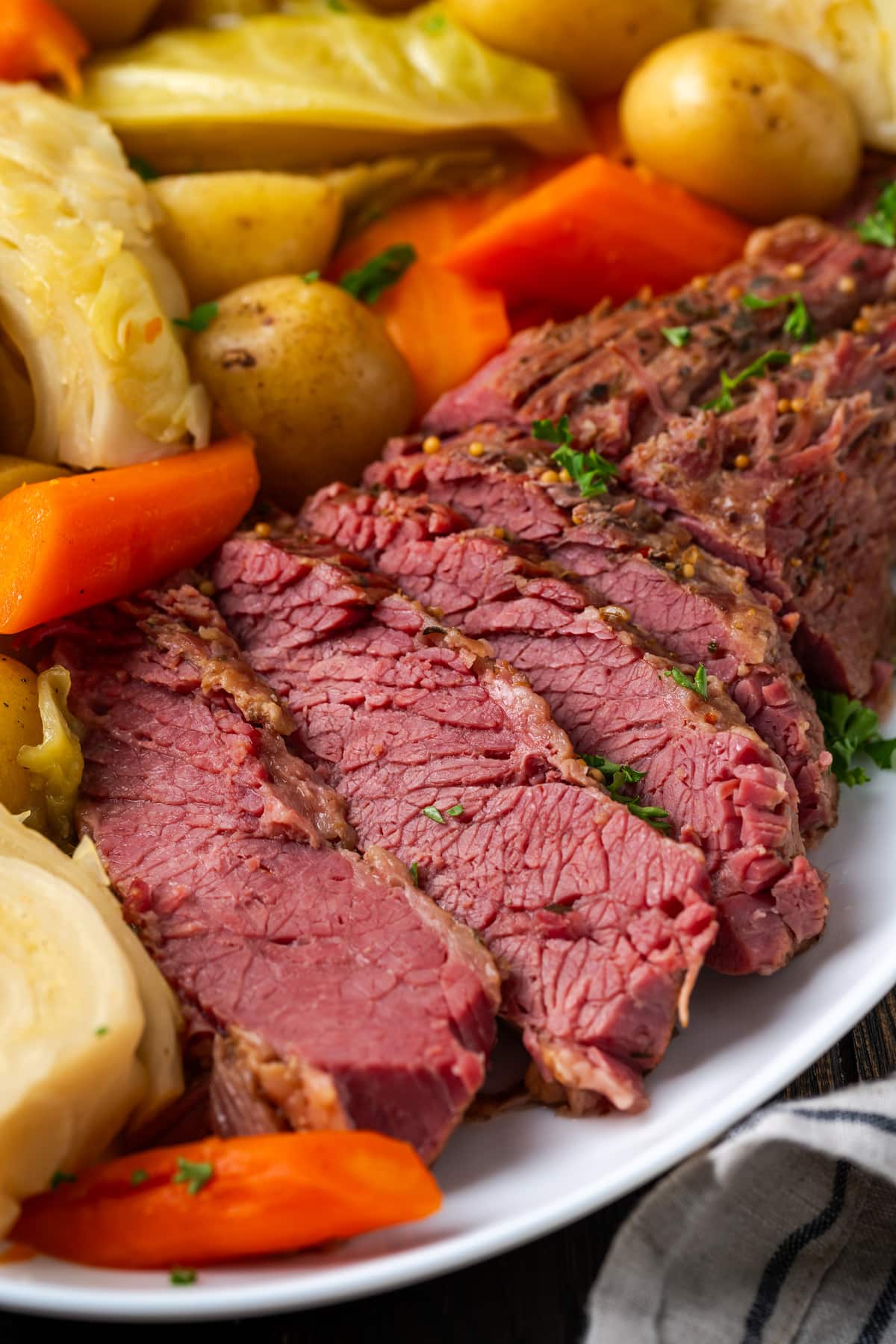 Sliced corned beef on a plate next to cabbage, potatoes, and carrots.