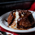 Chocolate Lava Cake topped with whipped cream and hot fudge melting from the inside on a white plate.
