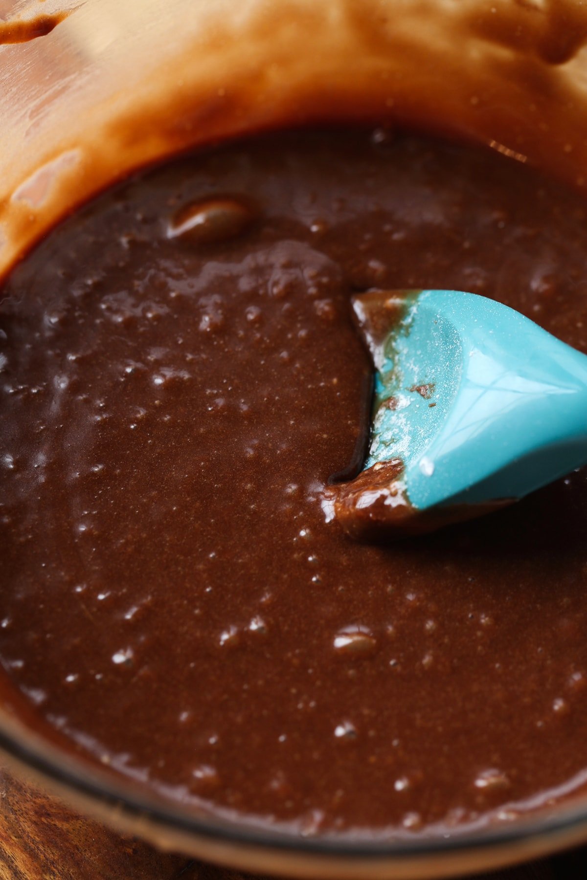 Chocolate cake batter in a mixing bowl with a blue rubber spatula mixing it.