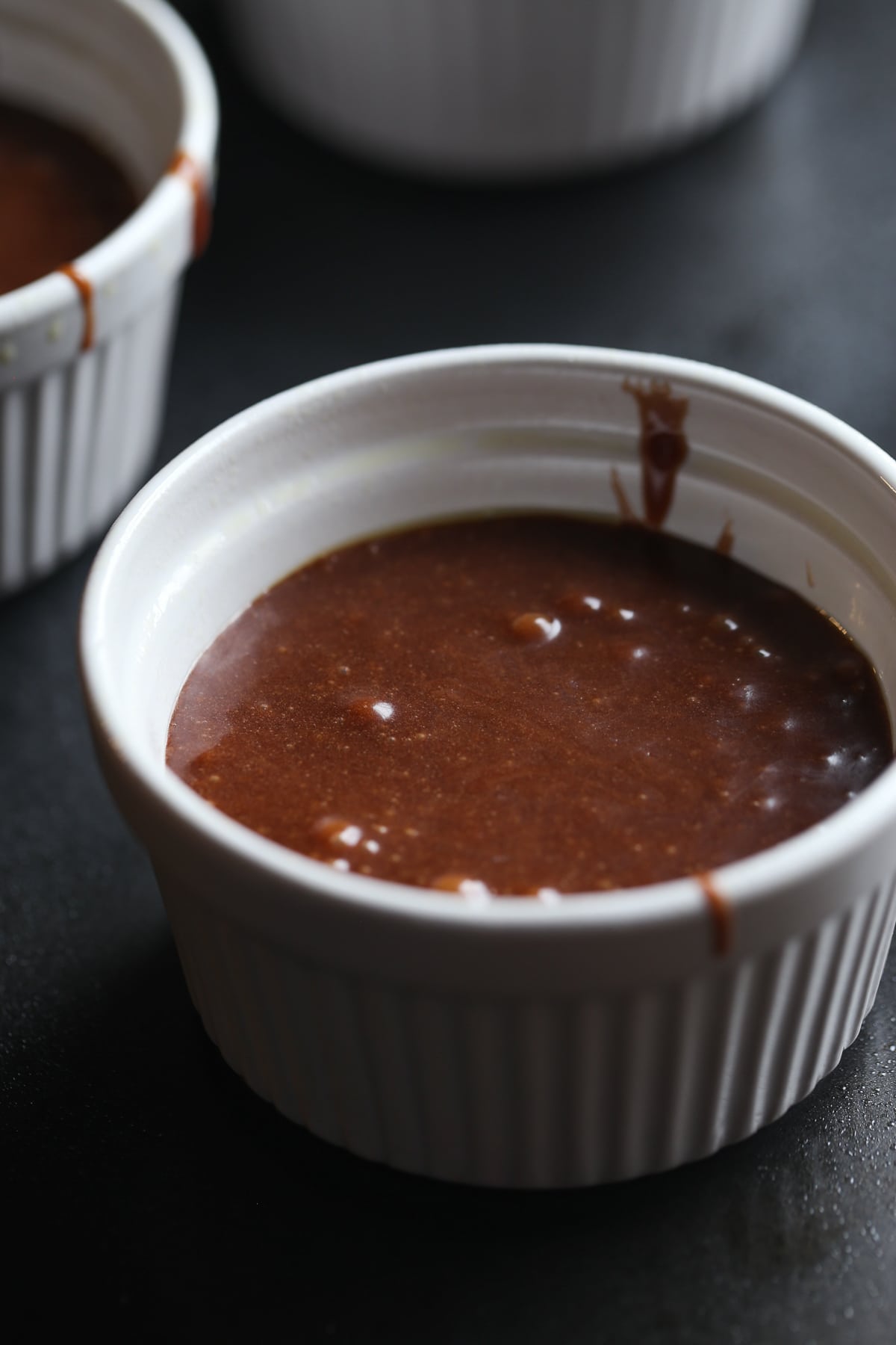 A white ramekin with chocolate cake batter inside before going into the oven.