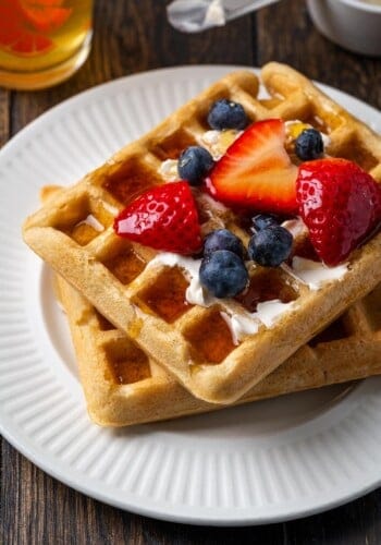Two waffles topped with syrup, fresh strawberries, and blueberries on a white plate.