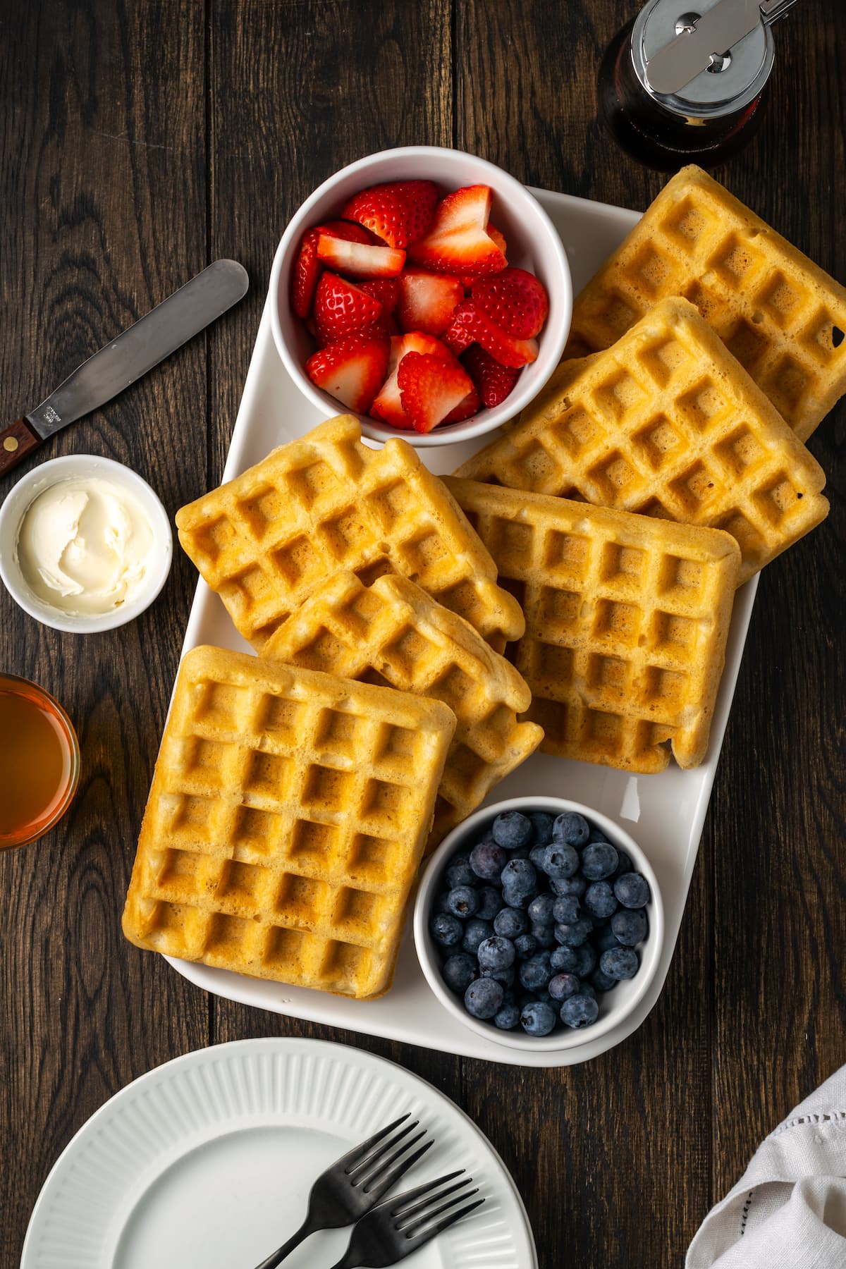 Overhead view of a platter of waffles served with bowls of blueberries and strawberries.