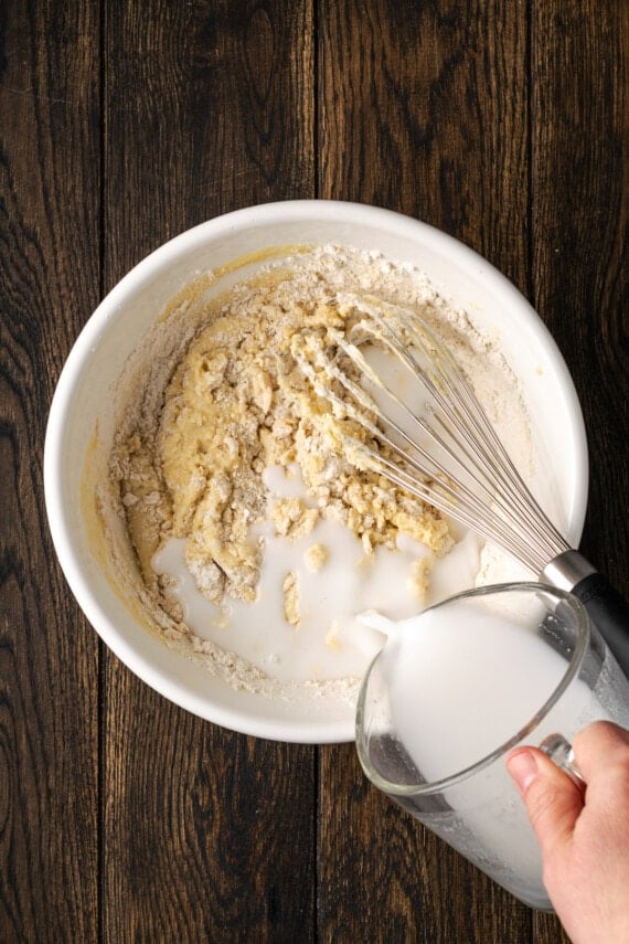Additional milk added to waffle batter ingredients in a bowl.