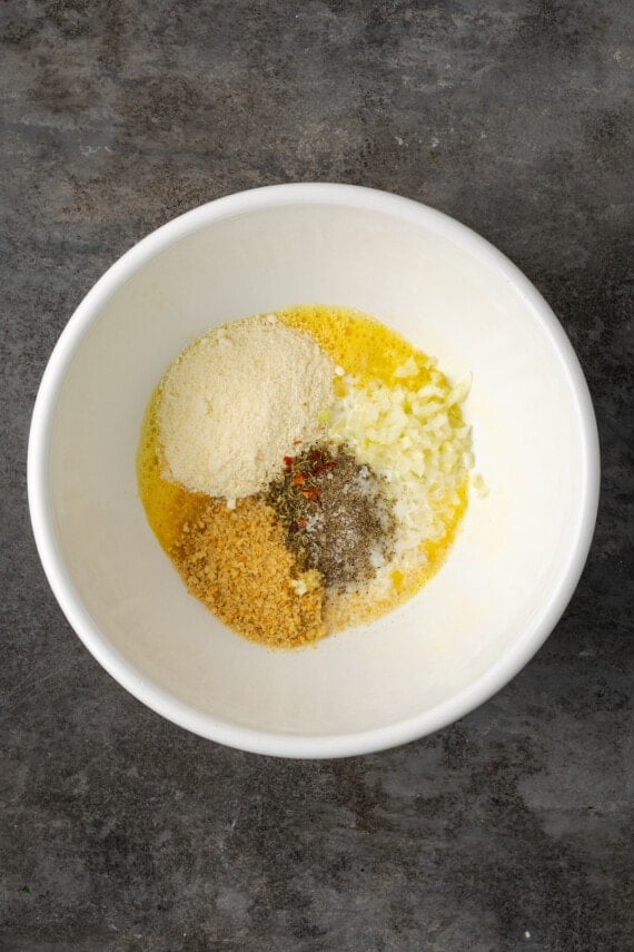 Seasonings, breadcrumbs, and parmesan cheese added to a bowl with a beaten egg and milk.