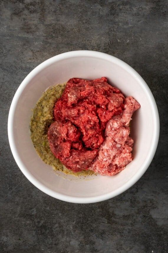 Ground beef and ground pork added to a bowl with meatball binding ingredients.