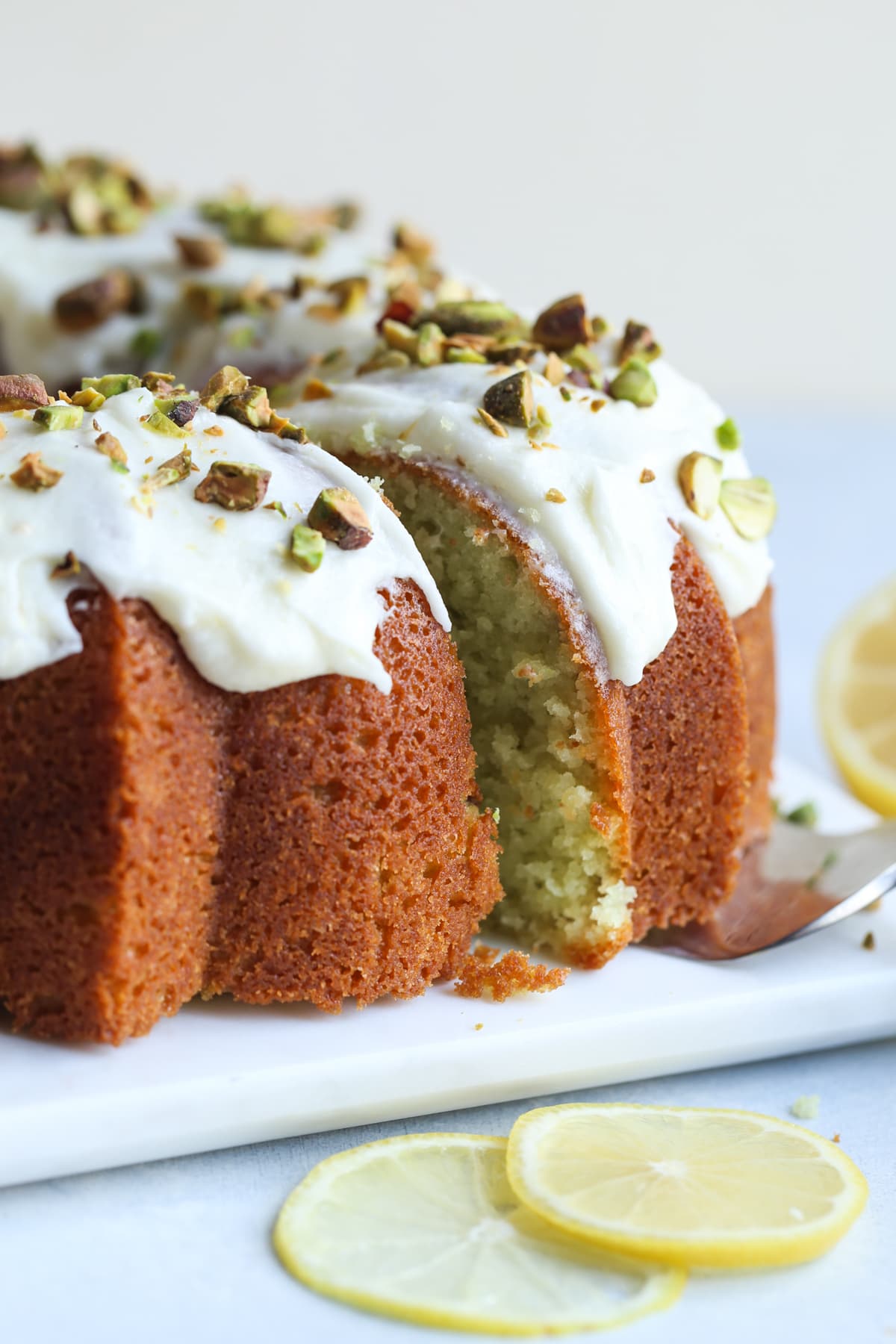 Slicing a piece of pistachio bundt cake topped with icing and chopped pistachios