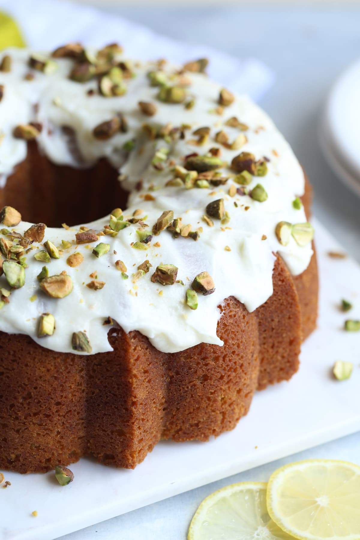 Pistachio Bundt Cake topped with white icing and chopped pistachios on a white serving plate.