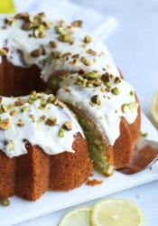 Frosted pistachio lemon bundt cake garnished with crushed pistachios on a square plate with a slice being served.