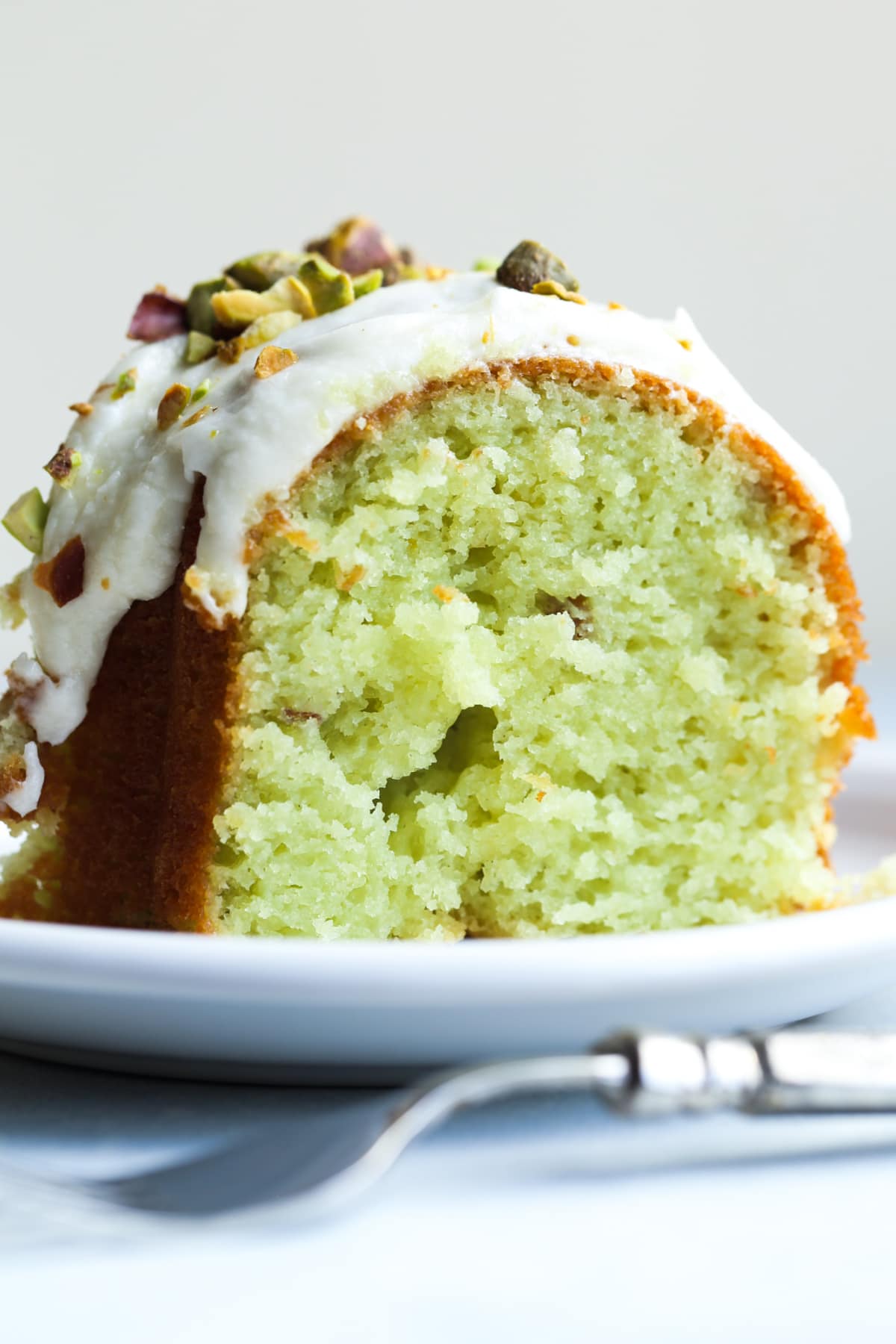 A slice of green pistachio cake on a white plate