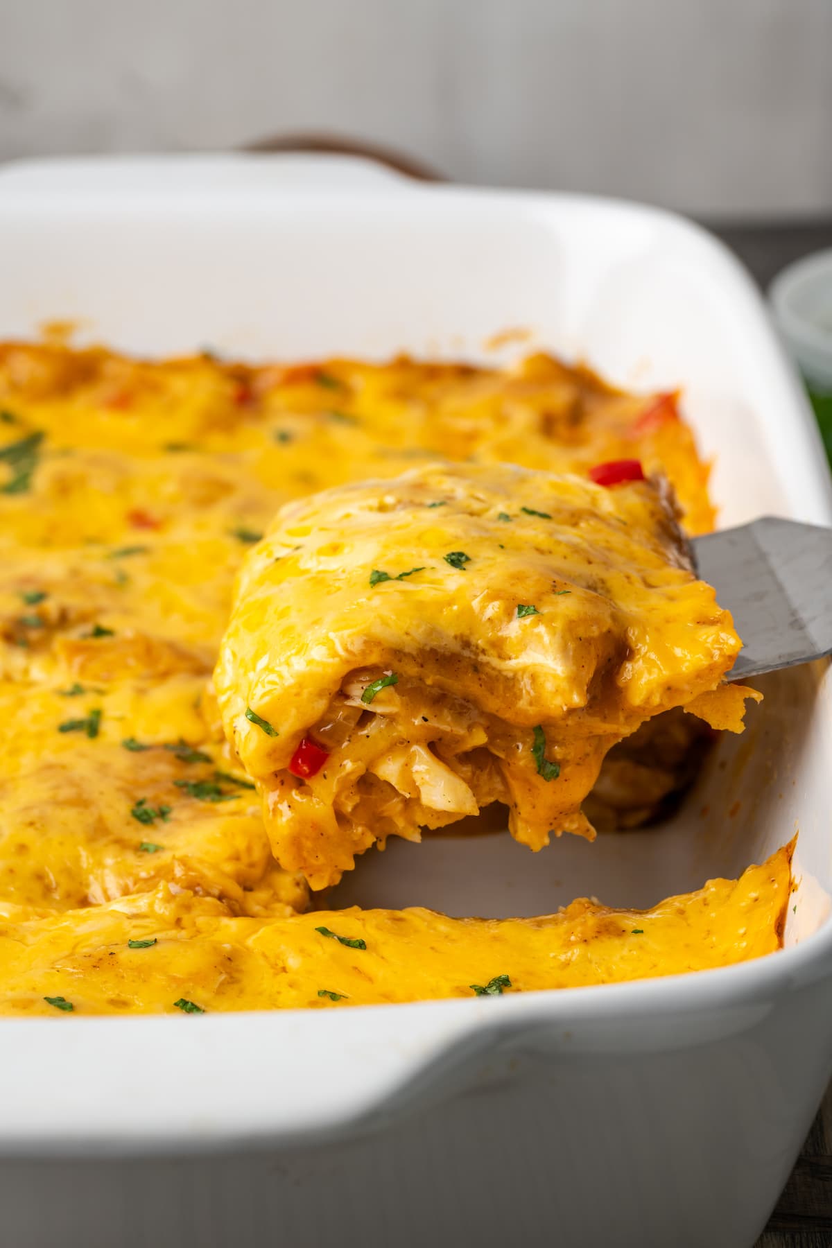 A slice of King Ranch chicken is lifted from a casserole dish.