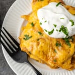 Overhead view of a serving of King Ranch chicken topped with sour cream on a plate next to a fork.
