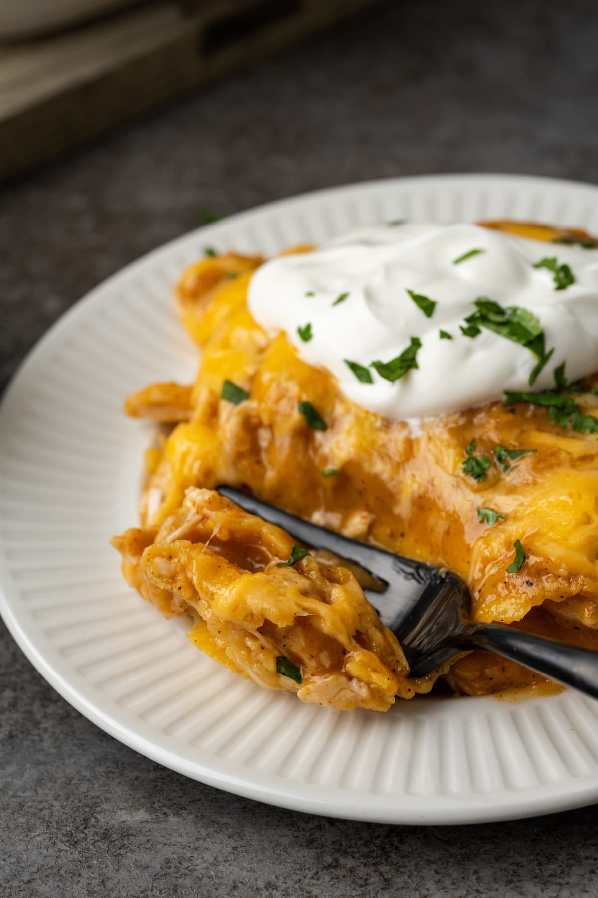 A fork cuts into a serving of Kinch Ranch chicken topped with sour cream on a plate.
