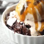 Brownie pudding served in a ramekin with vanilla ice cream and a drizzle of caramel sauce.