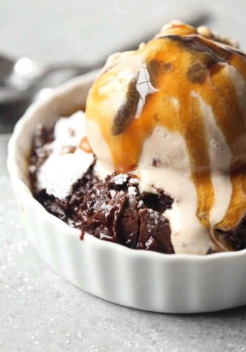 Brownie pudding served in a ramekin with vanilla ice cream and a drizzle of caramel sauce.