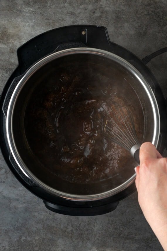 This juicy Instant Pot pork loin is smothered with a savory spice rub and out-of-this-world tender. Sear and cook your pork all in one pot! A hand using a whisk to stir a cornstarch slurry into the cooking liquid inside the instant pot.