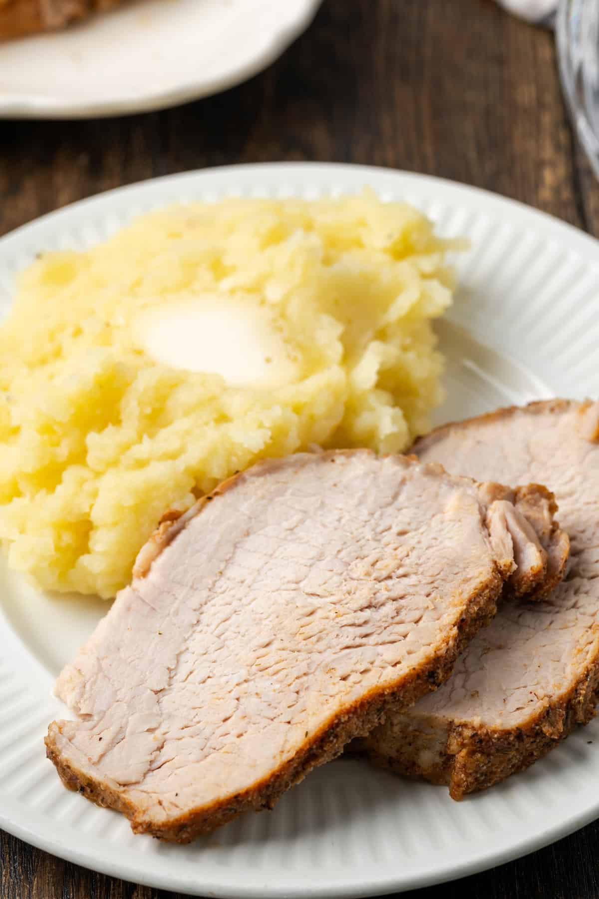 This juicy Instant Pot pork loin is smothered with a savory spice rub and out-of-this-world tender. Sear and cook your pork all in one pot! Two slices of instant pot pork loin next to a side of mashed potatoes on a white plate.