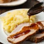 Two slices of instant pot pork loin being drizzled with gravy next to a side of mashed potatoes on a white plate.