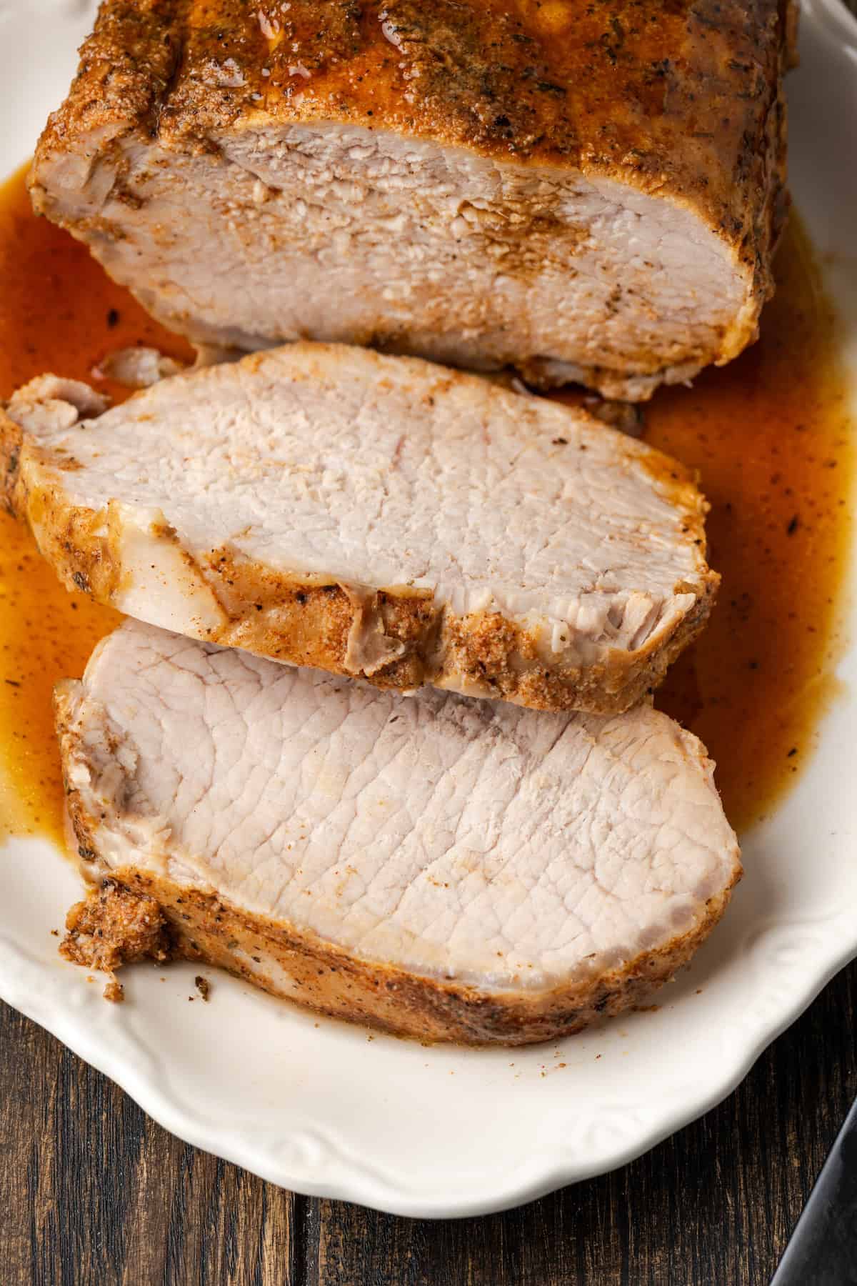 This juicy Instant Pot pork loin is smothered with a savory spice rub and out-of-this-world tender. Sear and cook your pork all in one pot! Overhead view of instant pot pork loin covered with sauce and sliced on a white platter.