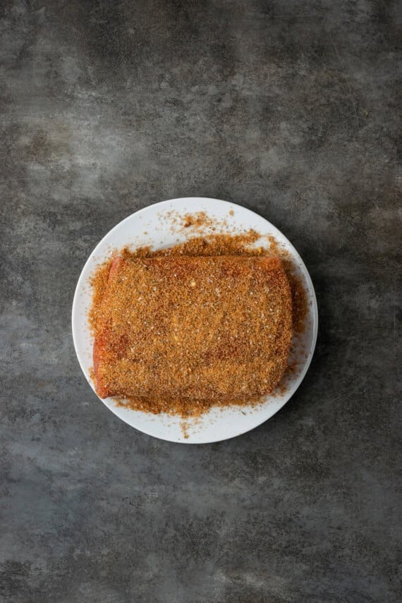 This juicy Instant Pot pork loin is smothered with a savory spice rub and out-of-this-world tender. Sear and cook your pork all in one pot! Pork loin roast rubbed with seasoning on a white plate.