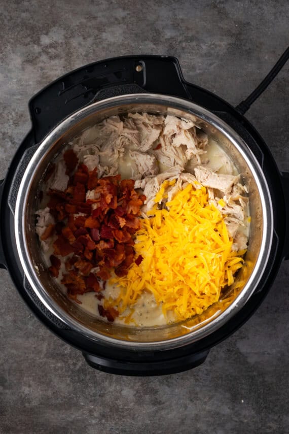 Shredded chicken, diced bacon, and shredded cheese added to the cream cheese sauce inside the instant pot.