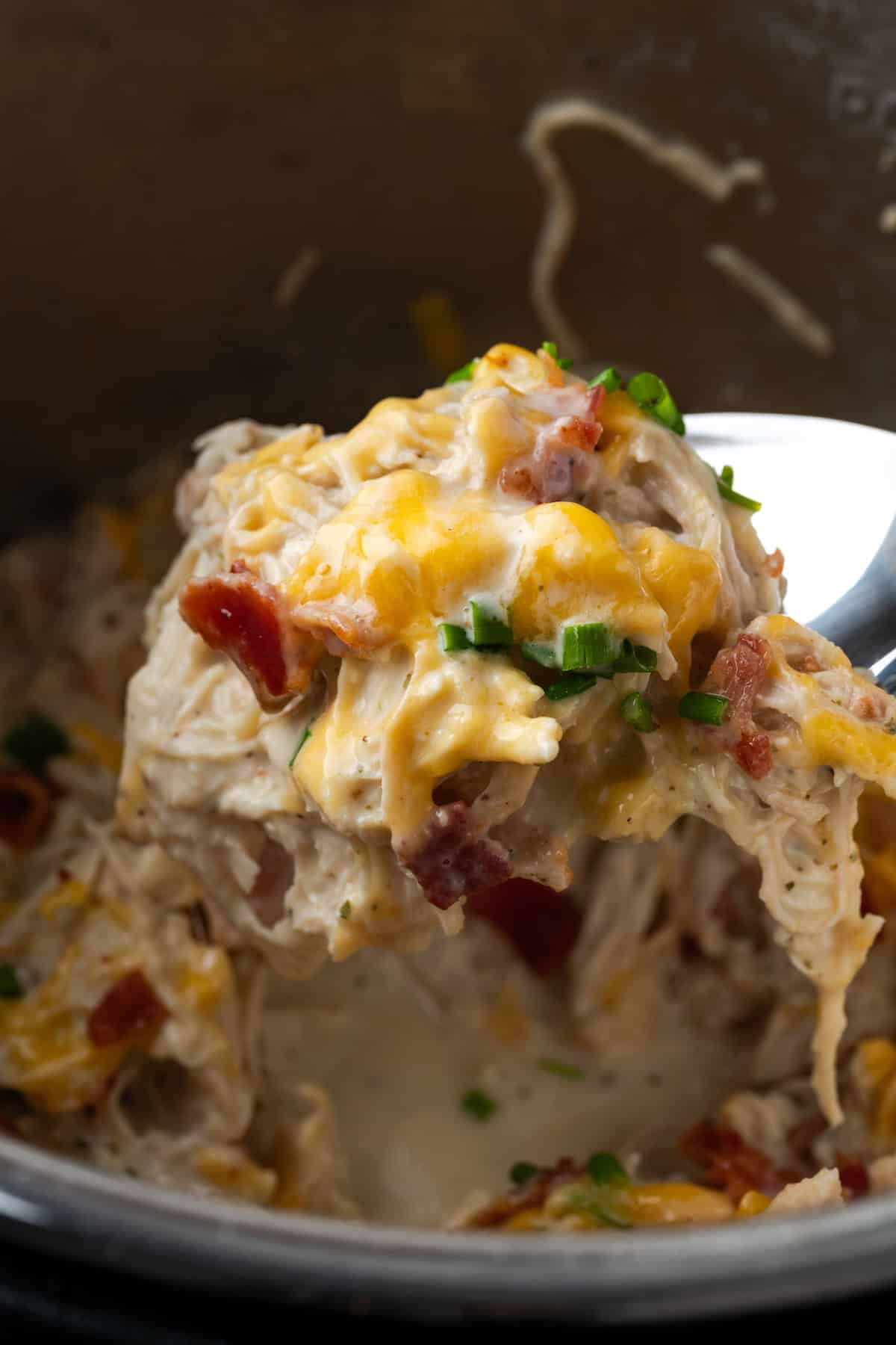 A spoon lifting a serving of crack chicken from the instant pot.