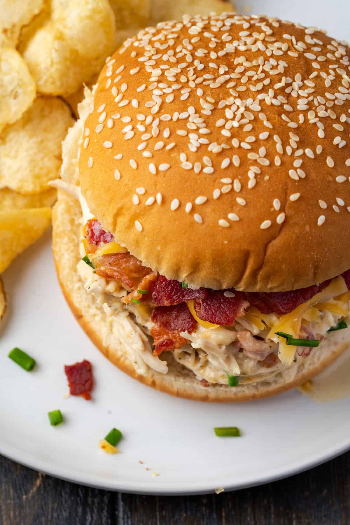 Close up overhead view of a crack chicken sandwich on a plate next to potato chips.